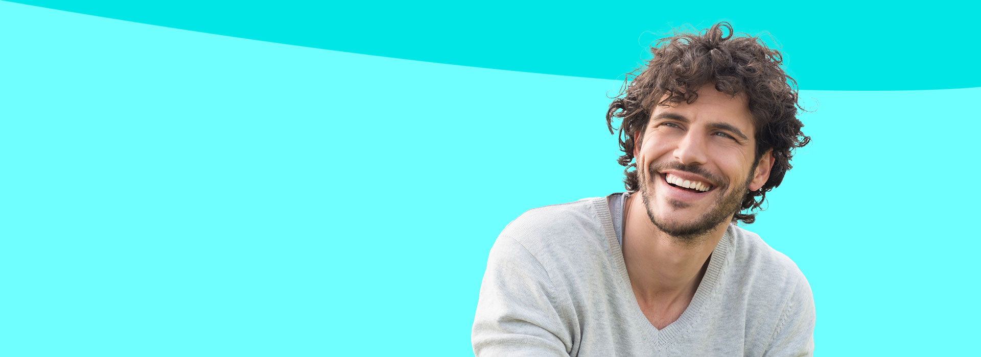 The image shows a man with curly hair, wearing a light-colored shirt, smiling and looking directly at the camera. He is standing against a bright blue background.