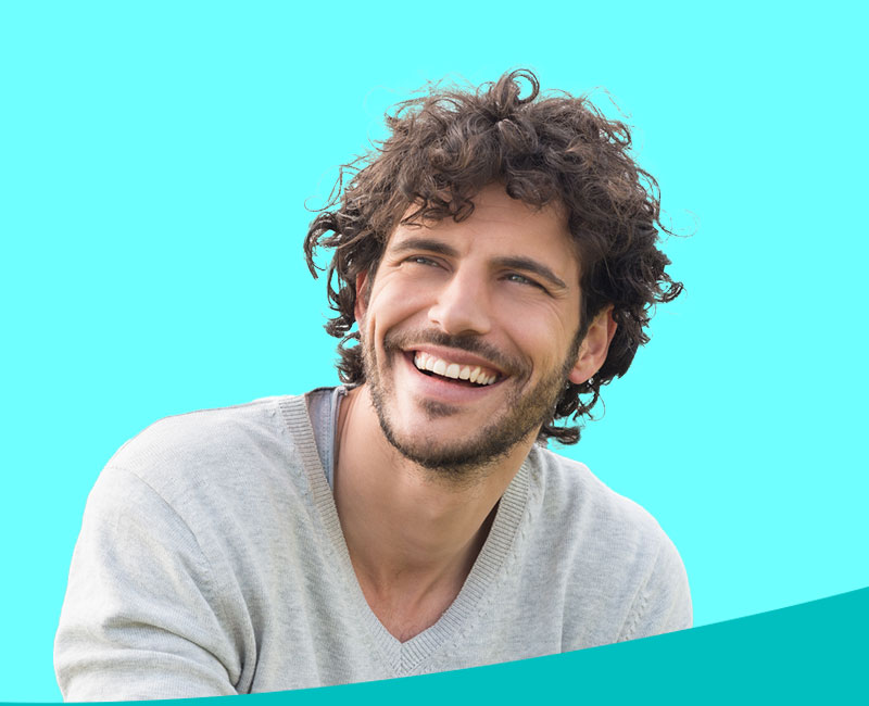 A man with curly hair and a beard, smiling broadly, against a plain blue background.