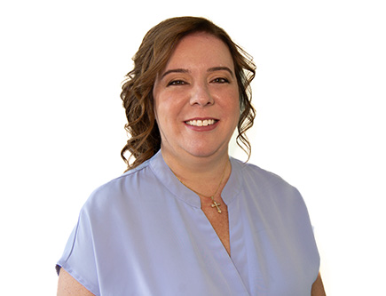 The image shows a woman with a smile, wearing a blue shirt and standing against a white background.
