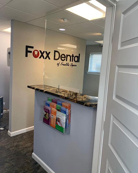 An interior view of a dental office reception area, featuring a sign for Fox Dental and a reception desk with informational pamphlets.