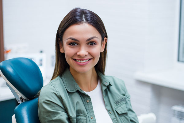 Smiling woman in dental office, wearing a green jacket and sitting in a dentist's chair.