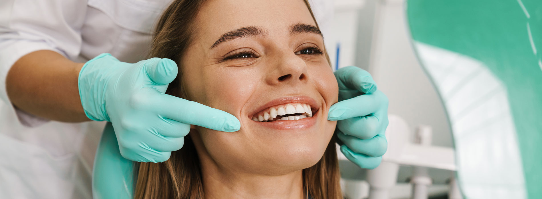 A woman receiving dental care, with a smile on her face and a dental hygienist's hands gently placed on her cheeks.