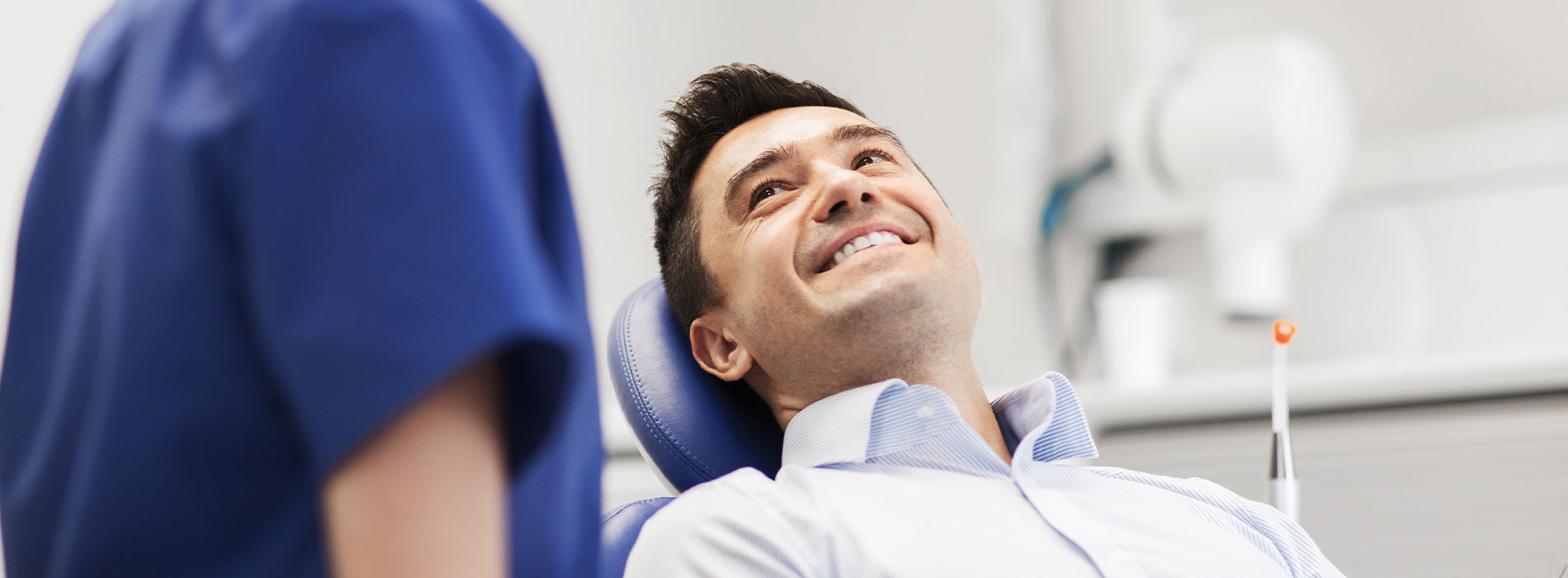 A man seated in a dental chair, smiling at the camera, with a dental professional standing next to him.