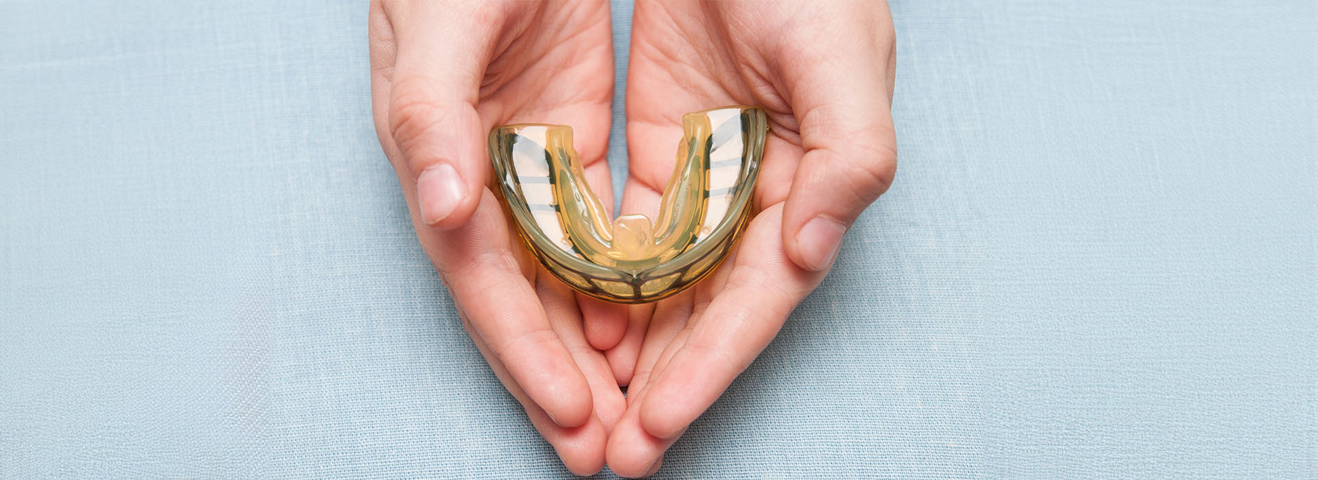 Hand holding a yellowish-gold object against a light blue background.