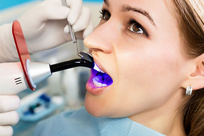 The image depicts a person receiving dental treatment, with a dentist using a dental drill and a purple mouthpiece to clean or repair teeth.