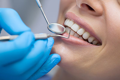 The image features a dental professional performing oral care on a patient's teeth, with the patient smiling and wearing a blue surgical gown.