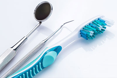 The image shows a collection of dental tools, including a toothbrush with blue bristles and a pair of scissors with a silver handle, placed on a white surface.