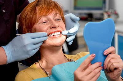 A woman in a dental chair receiving a teeth cleaning, with a dental professional holding a toothbrush to her mouth.