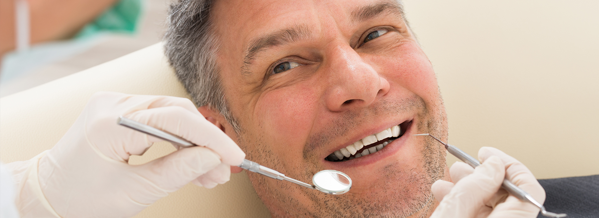 The image shows a man sitting in a dental chair, receiving dental treatment, with a dentist working on his teeth.