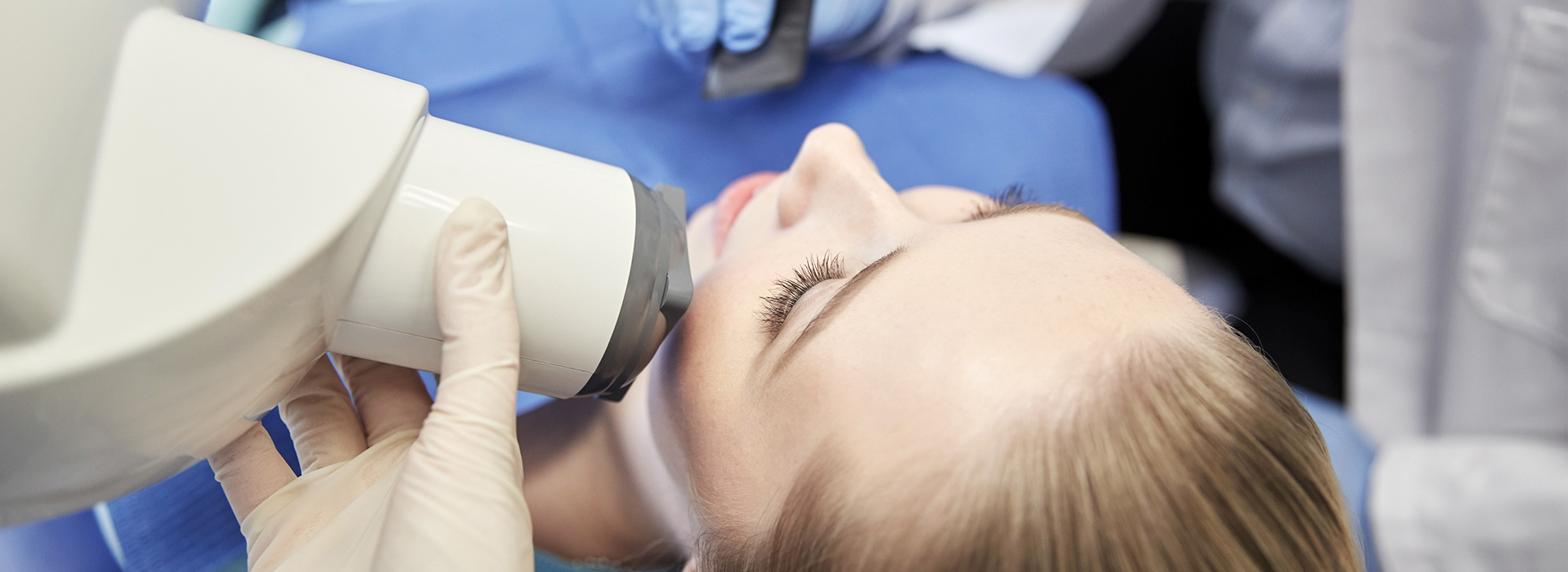 The image depicts a person receiving dental care, with a focus on the dental chair and the professional's hands working on their mouth.