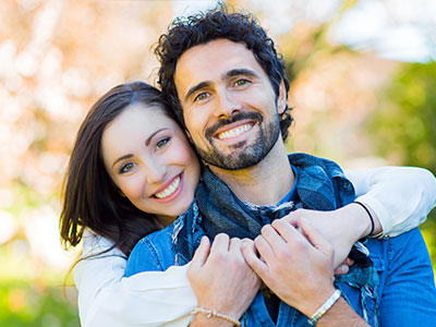 The image shows a man and a woman embracing each other, with the man smiling broadly at the camera.