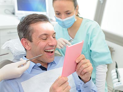 A man in a dental chair, holding up a pink card with a smile, as a woman in scrubs looks on.