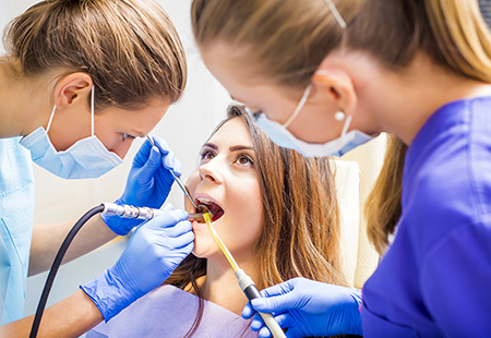 The image shows a dental care setting where a woman is seated in a dental chair, receiving dental treatment from a dentist.