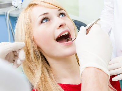 Woman undergoing dental procedure, smiling with mouth open, in chair with dental tools and gloves visible.